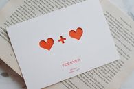 Top view of white paper postcard with cutout red hearts placed on top of opened novel book