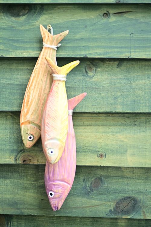 Free Three wooden fish hanging on a rustic green wall, creating an artistic display. Stock Photo