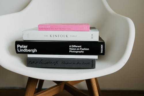 Composed stack of art and fashion books arranged on white comfortable chair in modern apartment