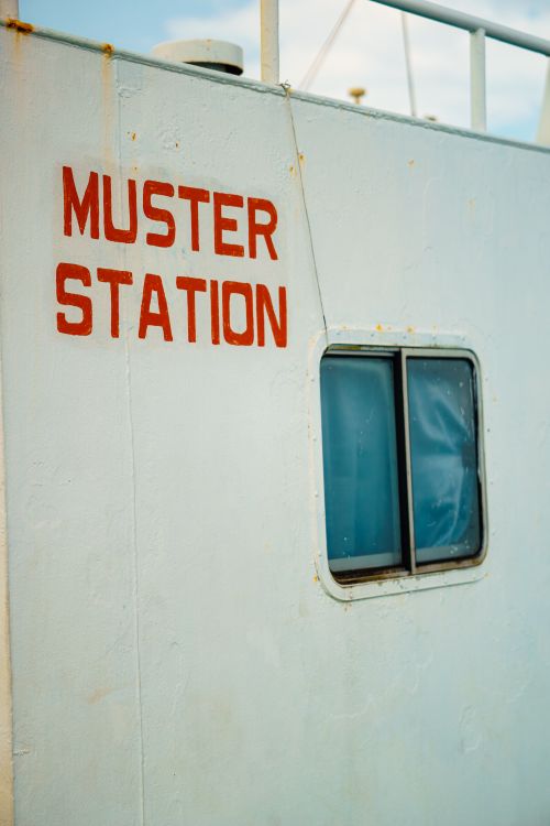 Free Close-up of a muster station sign on a ship's exterior with a small window. Stock Photo