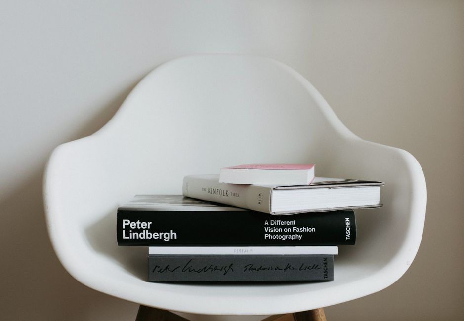 Comfortable white chair with arranged pile of various hardcover books placed near wall in modern light room