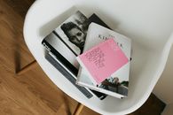 From above view of pile of different art and fashion books placed on white chair in modern apartment