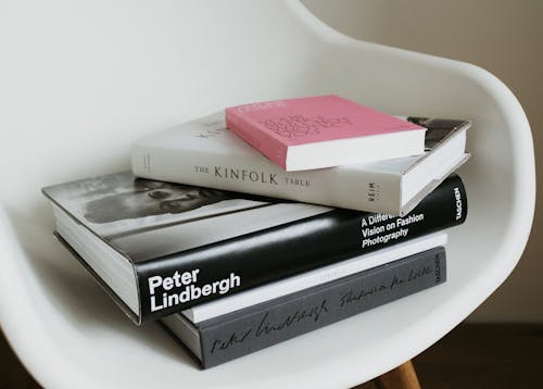 Free Arranged pile of modern art and fashion books from home collection placed on white chair near wall in modern light apartment Stock Photo