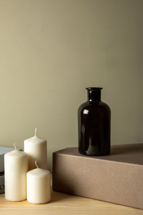 Free Elegant still life featuring candles, a brown bottle, and a textured box on a wooden surface. Stock Photo