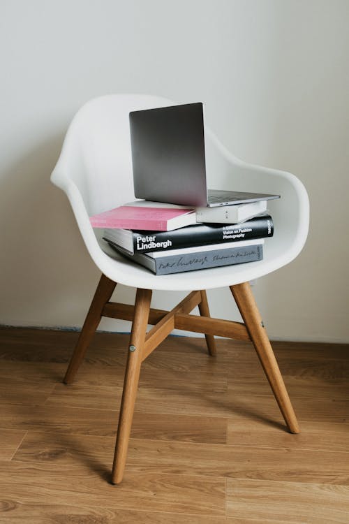 White chair with stack of books and laptop on top