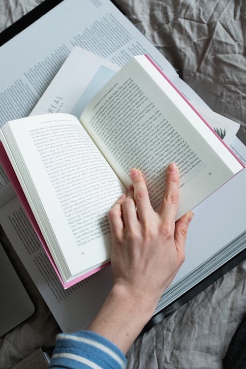 Free Top view of crop person reading various opened books while resting on soft blanket on comfortable bed in cozy bedroom at home Stock Photo