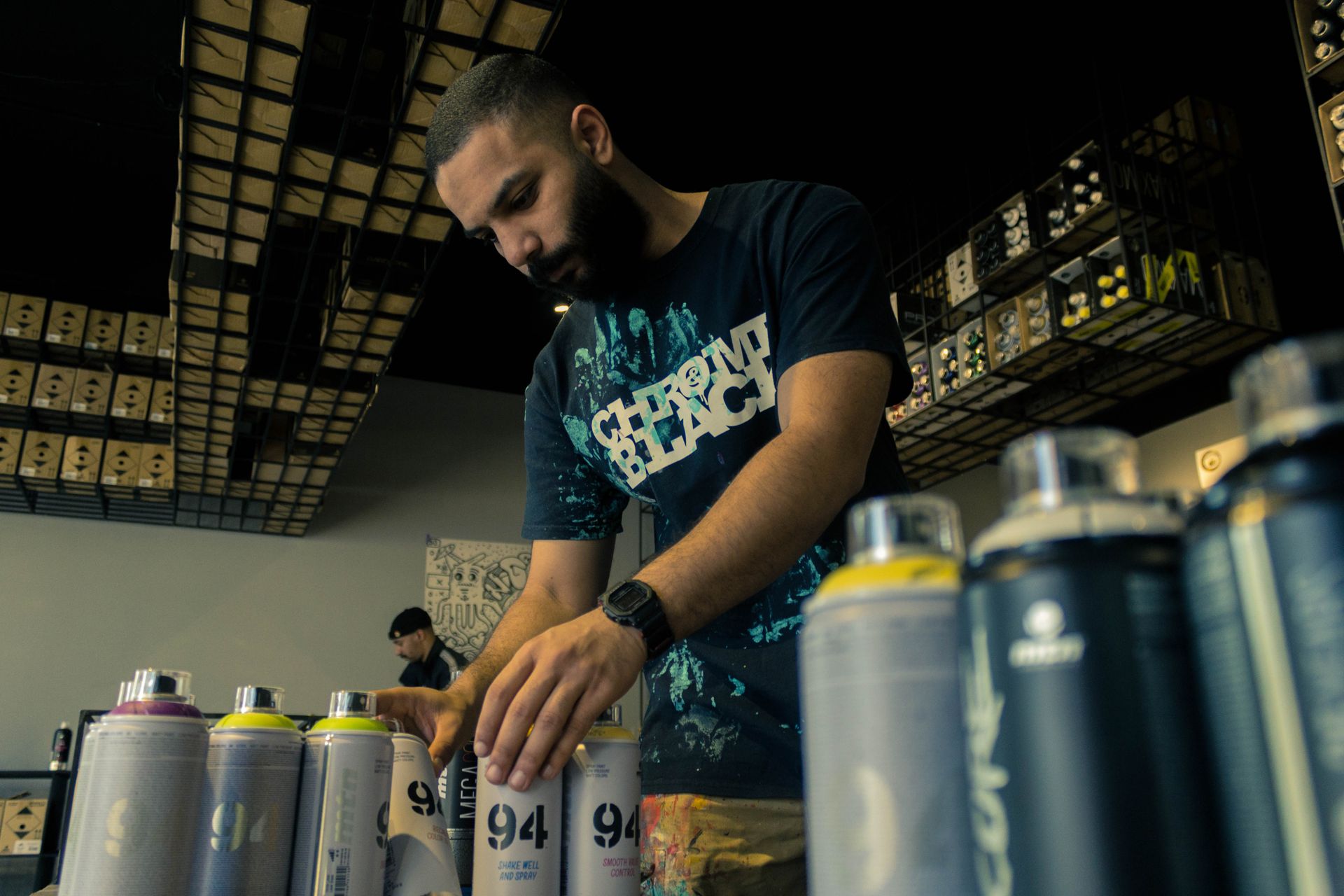 A store employee in Bahrain organizes spray paint cans on shelves indoors.