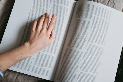 From above of crop anonymous female searching for information in article of book