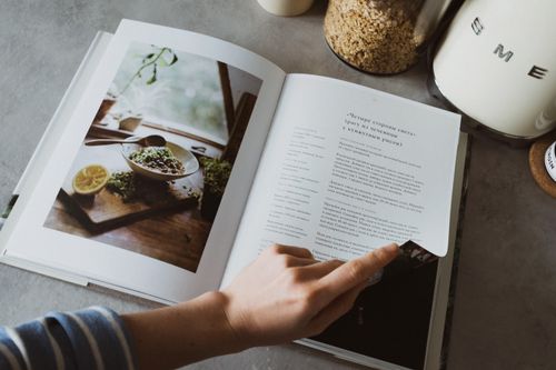 Free From above of crop faceless woman reviewing article in recipe book in kitchen Stock Photo