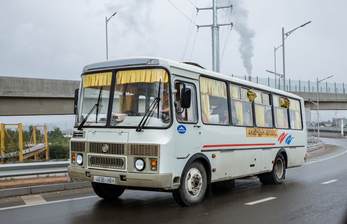 Free Local public bus with anonymous driver and passengers windshield driving on asphalt road with marking lines near cement bridge under cloudy sky with smoke Stock Photo