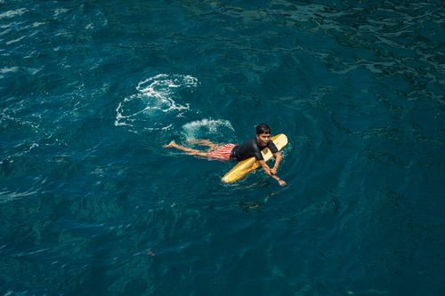 Free A young surfer paddles with a yellow board in clear blue ocean waters. Stock Photo