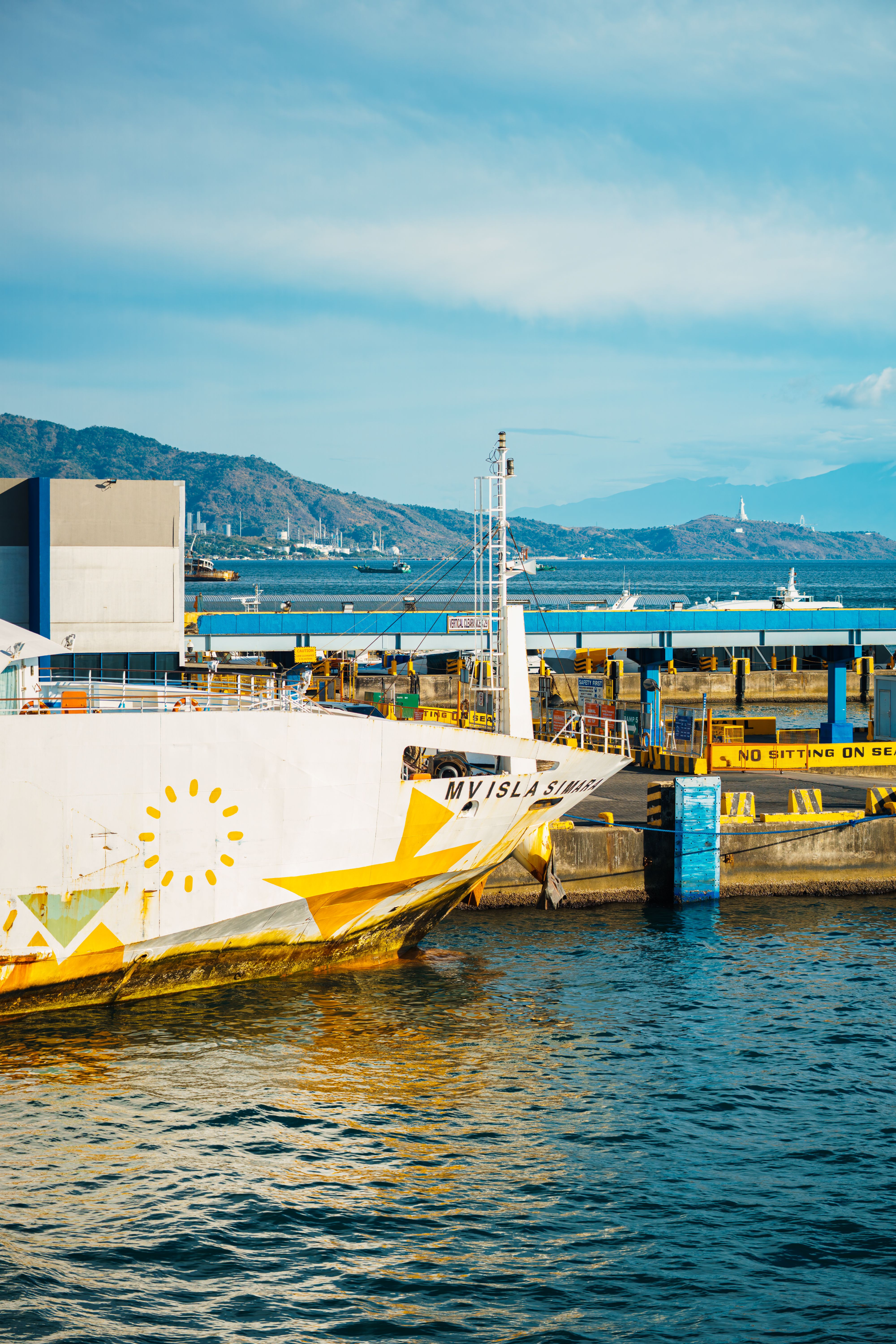 A vibrant ferry moored at a scenic harbor with mountainous backdrop under a clear blue sky.