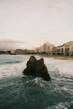 Stunning view of Biarritz coastline with city skyline and ocean waves crashing on rocks.