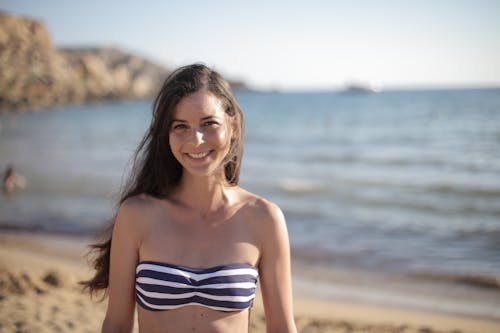 Free Woman in Black and White Stripe Bikini Top Standing on Beach Smiling Stock Photo