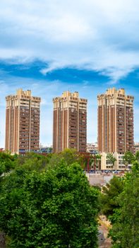 A striking view of three modern high-rise residential buildings surrounded by lush greenery on a clear day.