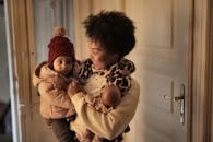 一位快乐的少数族裔妇女抱着孩子，拿着玩具站在房间里，准备出门时看了看婴儿的衣服