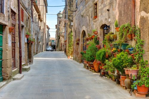 Free A picturesque alley in Tuscany lined with medieval buildings and potted plants. Stock Photo