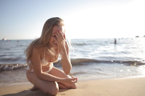 Free Young happy female with blond hair in bikini enjoying spending time on sandy beach Stock Photo