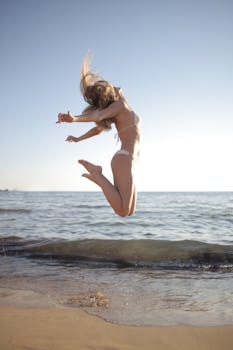 Side view of young glad female with blond hair cheerfully jumping on empty sandy beach