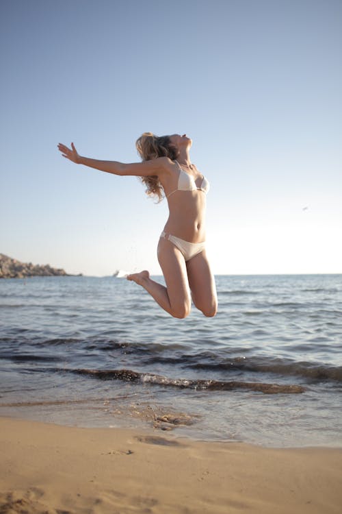 Young happy female with blond hair in bikini having fun on empty sandy beach
