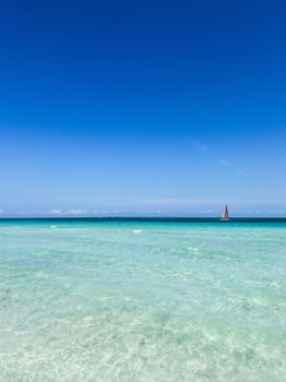 Peaceful blue Caribbean waters with a distant sailboat on a sunny day.