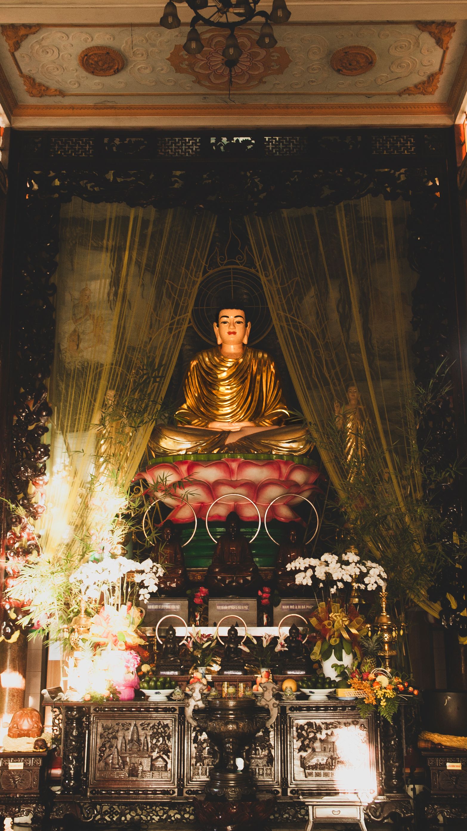 A stunning golden Buddha statue in a temple in Ho Chi Minh City, adorned with flowers and religious decor.