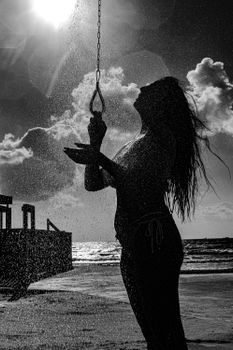 Dramatic black and white silhouette of a woman rinsing under a beach shower with ocean view.