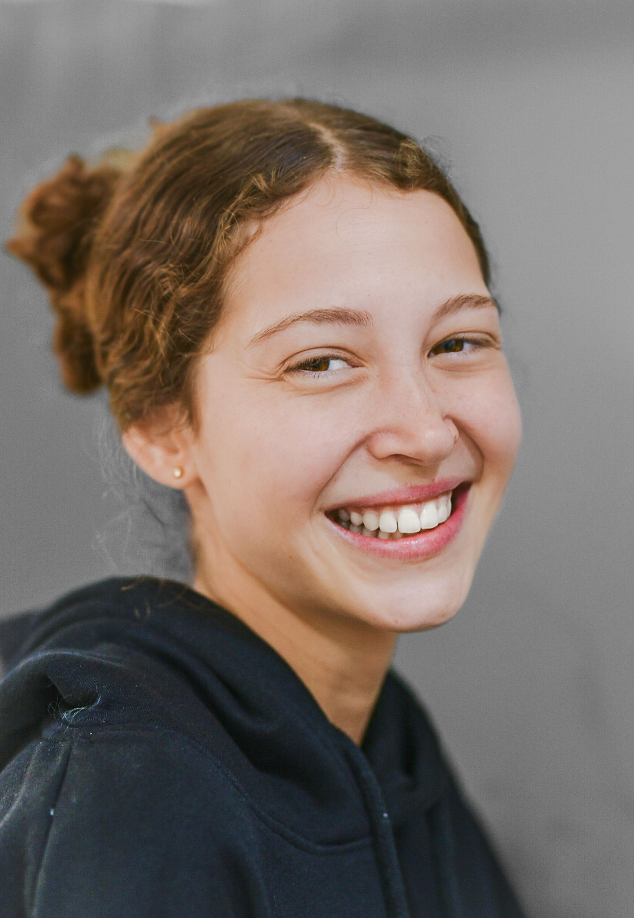 Cheerful young woman smiling in a hoodie against a plain background.