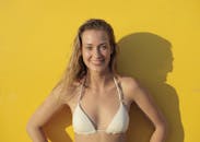 一位穿着比基尼、面带微笑的女人，站在亮黄色背景前