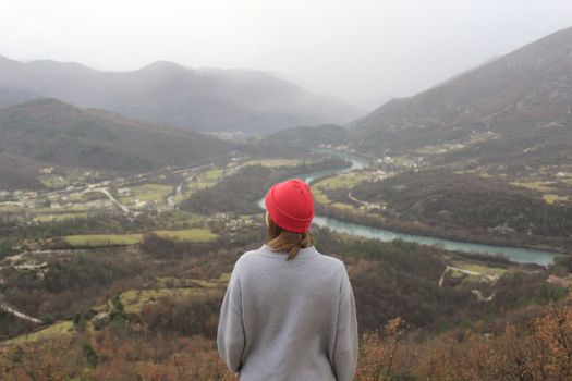 A woman in a red hat overlooking a vast mountain valley and winding river.