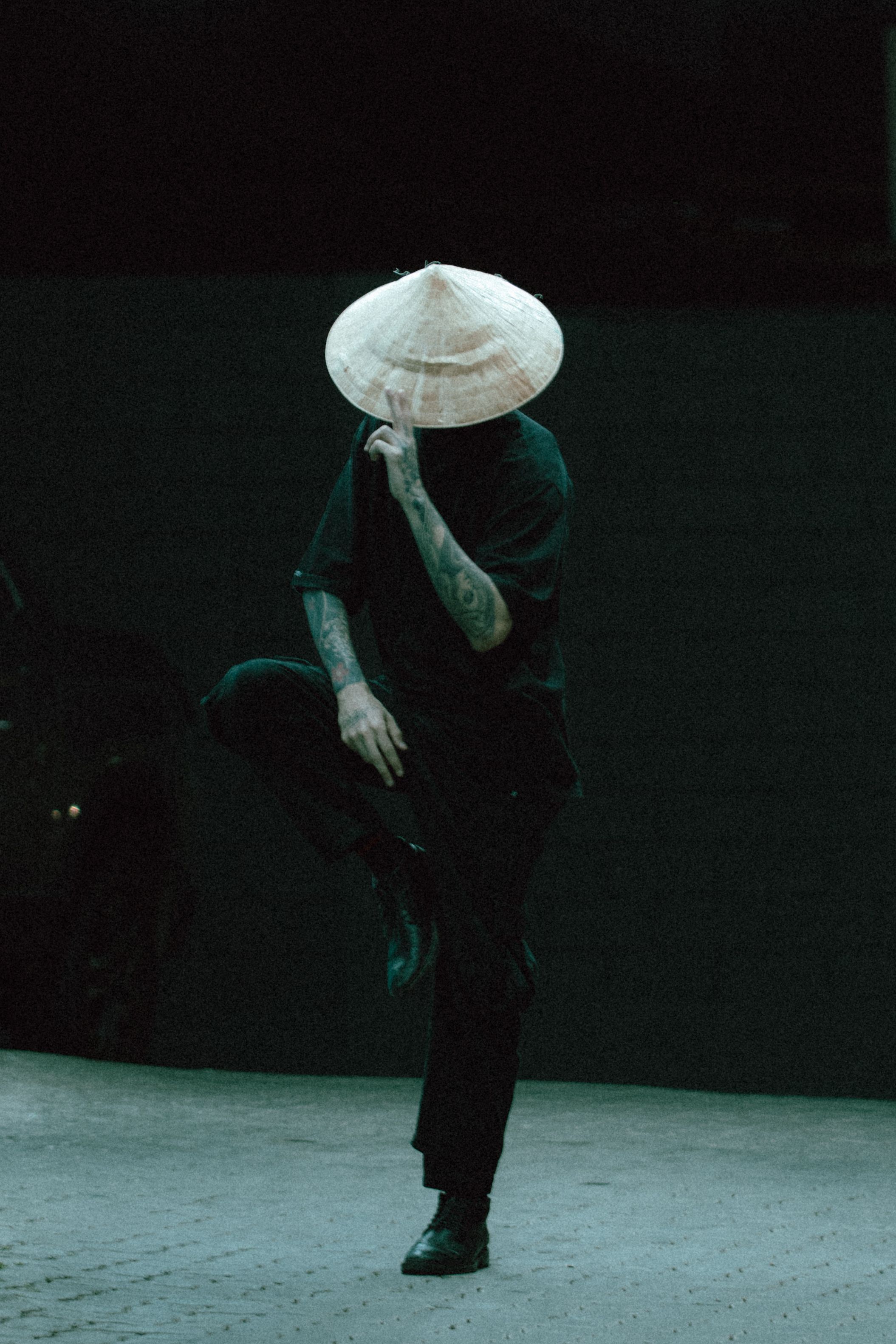 A person in a traditional Asian hat striking a pose in dim lighting.