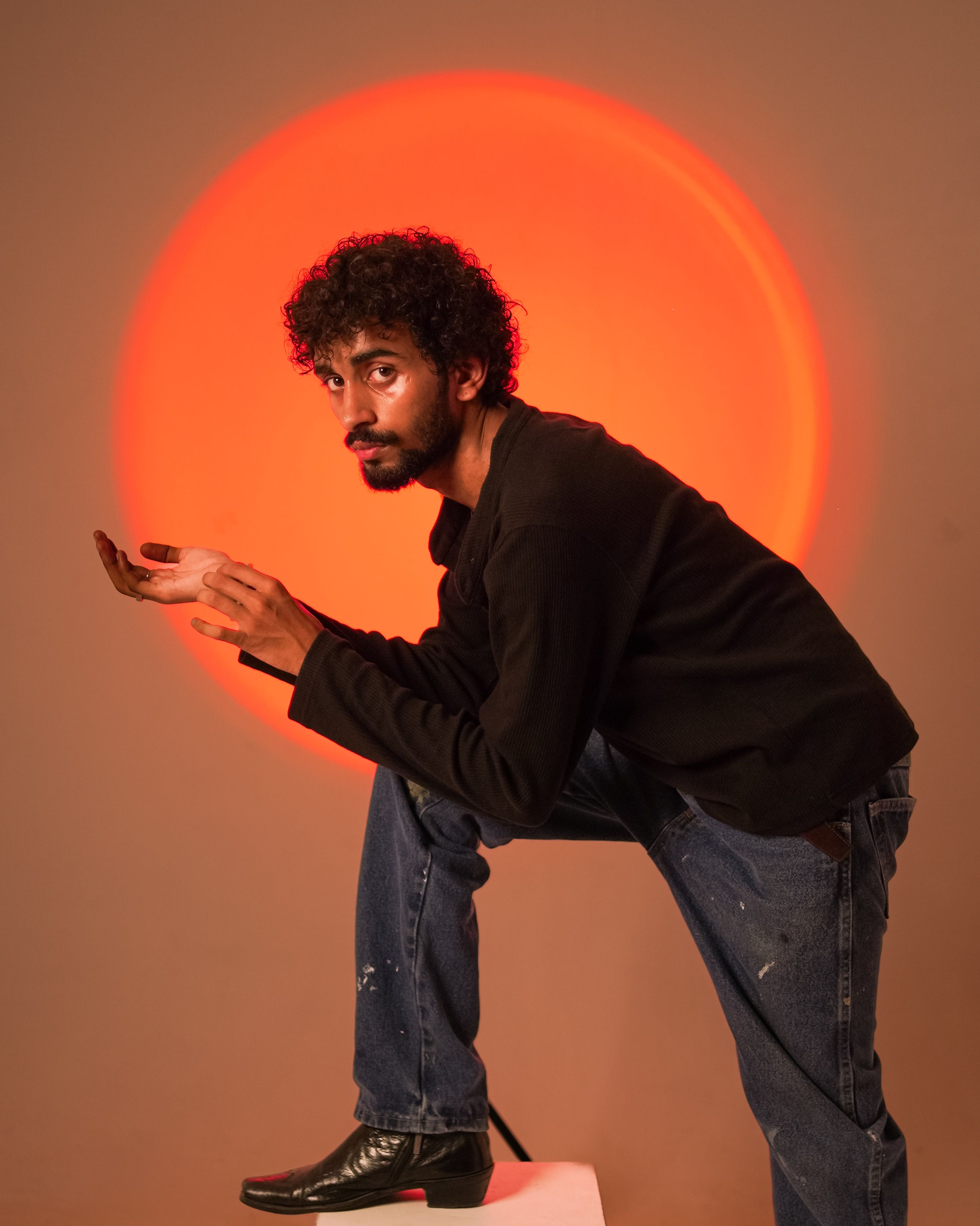 Dramatic portrait of a man posing with a vibrant orange circle backdrop, highlighting a moody atmosphere.