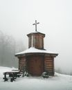 一座宁静的木制教堂，坐落在冬日雾霭之中，四周是白雪覆盖的树木
