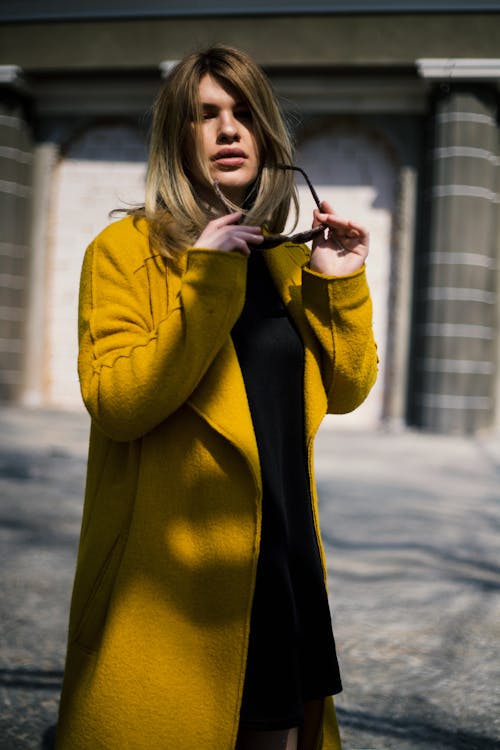 Woman In Yellow Coat Holding Sunglasses