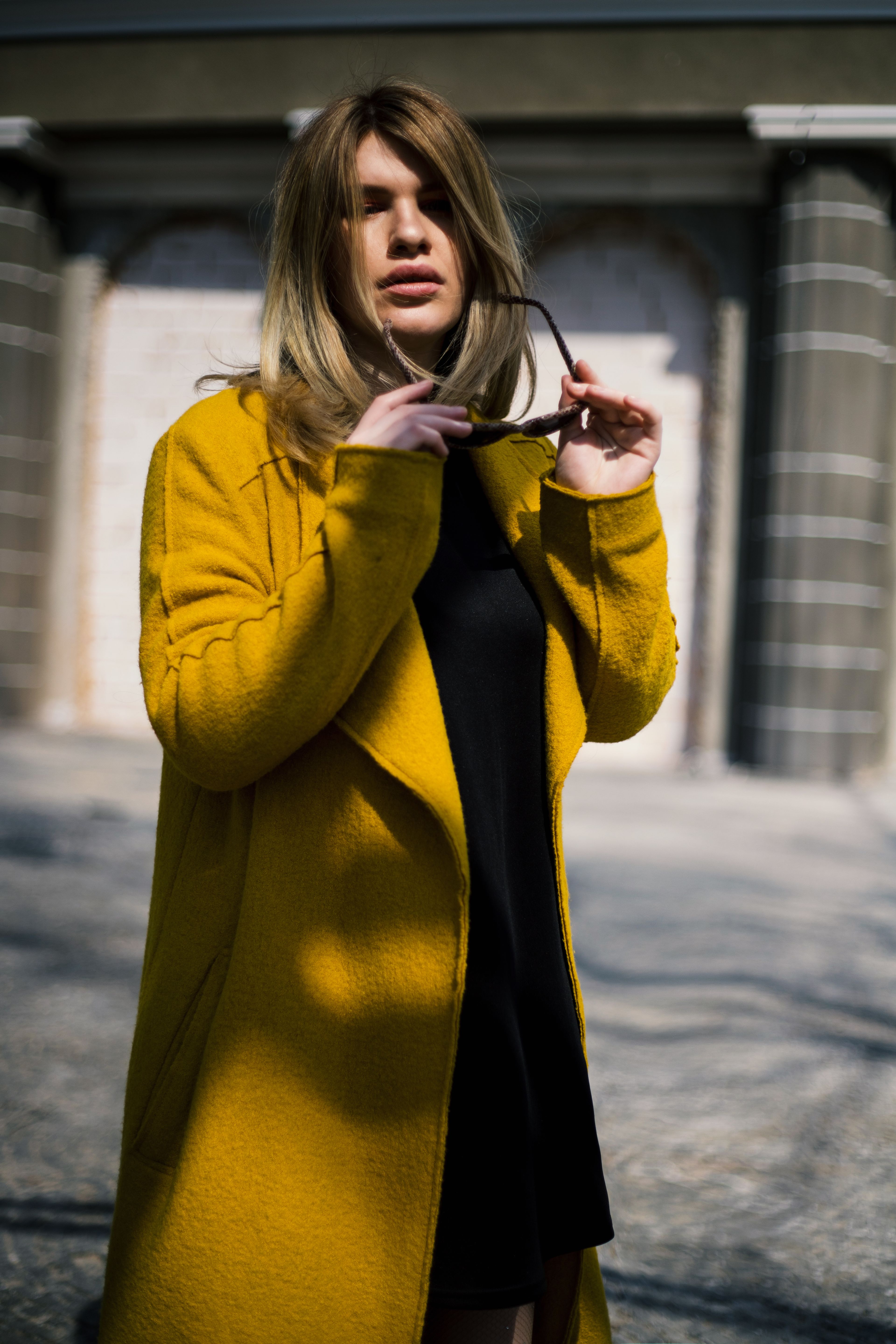 A woman in a yellow coat holding her sunglasses