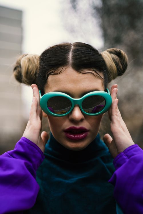 Free Stylish woman with unique hairstyle wearing green sunglasses and purple top outdoors. Stock Photo