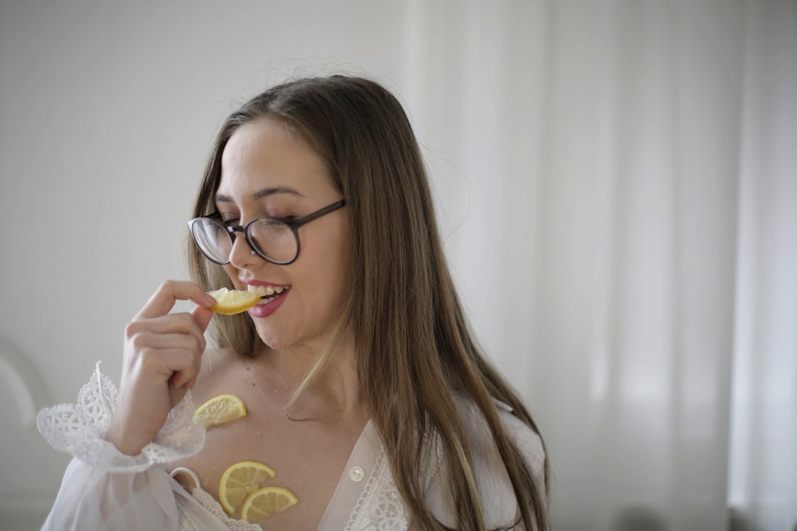 Woman In White Long Sleeve Shirt Wearing Eyeglasses Eating  Fruit