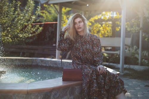 Elegant model with stylish handbag sitting near fountain