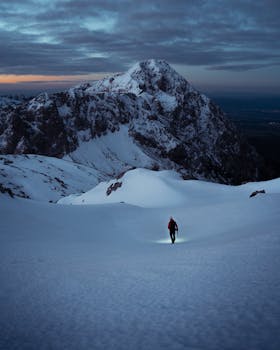Solo hiker with headlamp treks snowy Slovenian mountains at dawn.