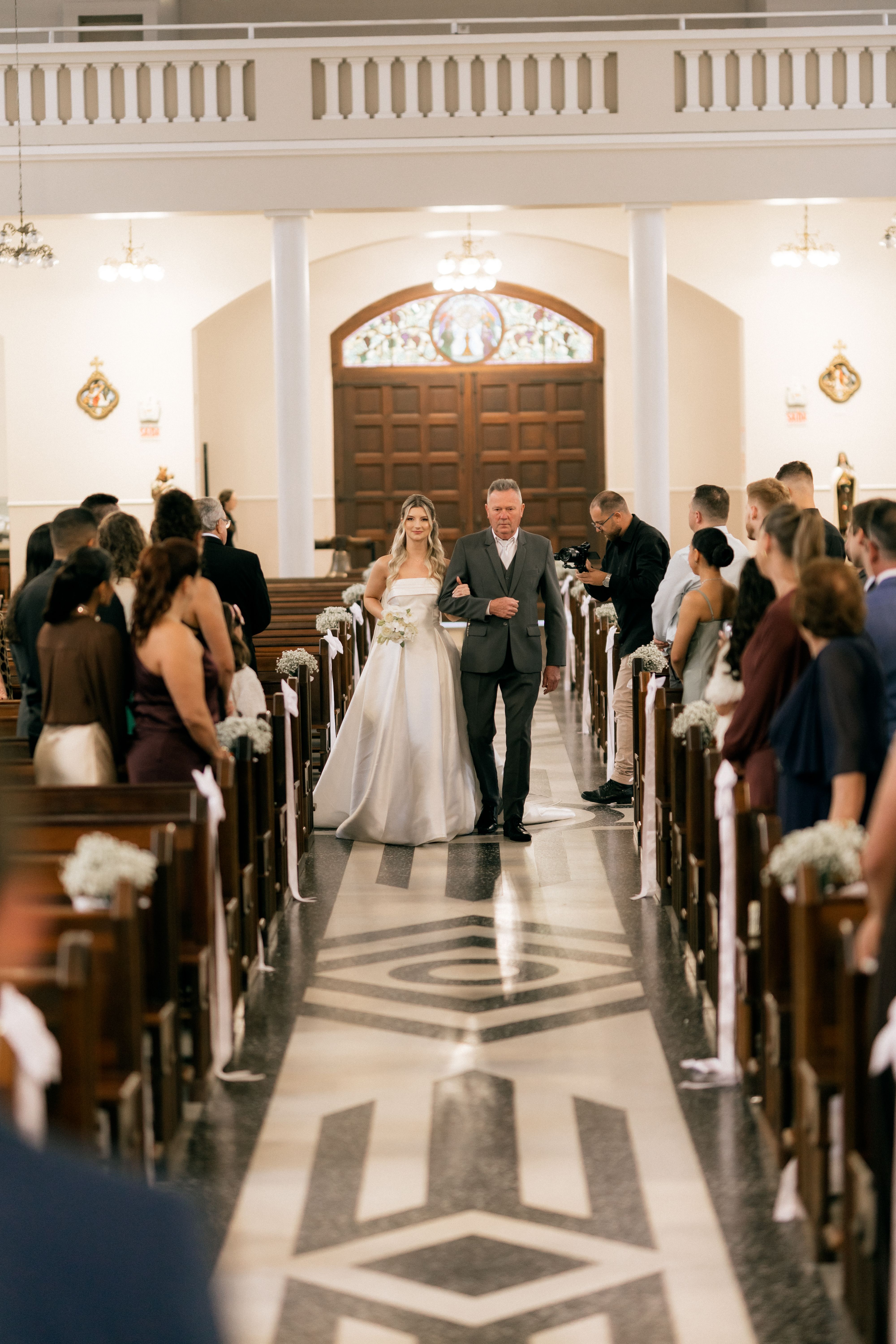 Elegant wedding ceremony in a church, capturing a bride and her escort walking down the aisle.