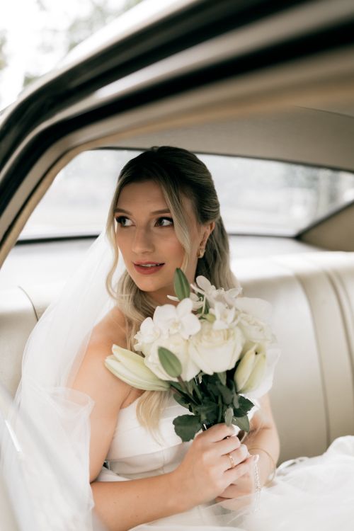 Free Stunning bride with white bouquet sits in a classic car, exuding elegance and grace. Stock Photo