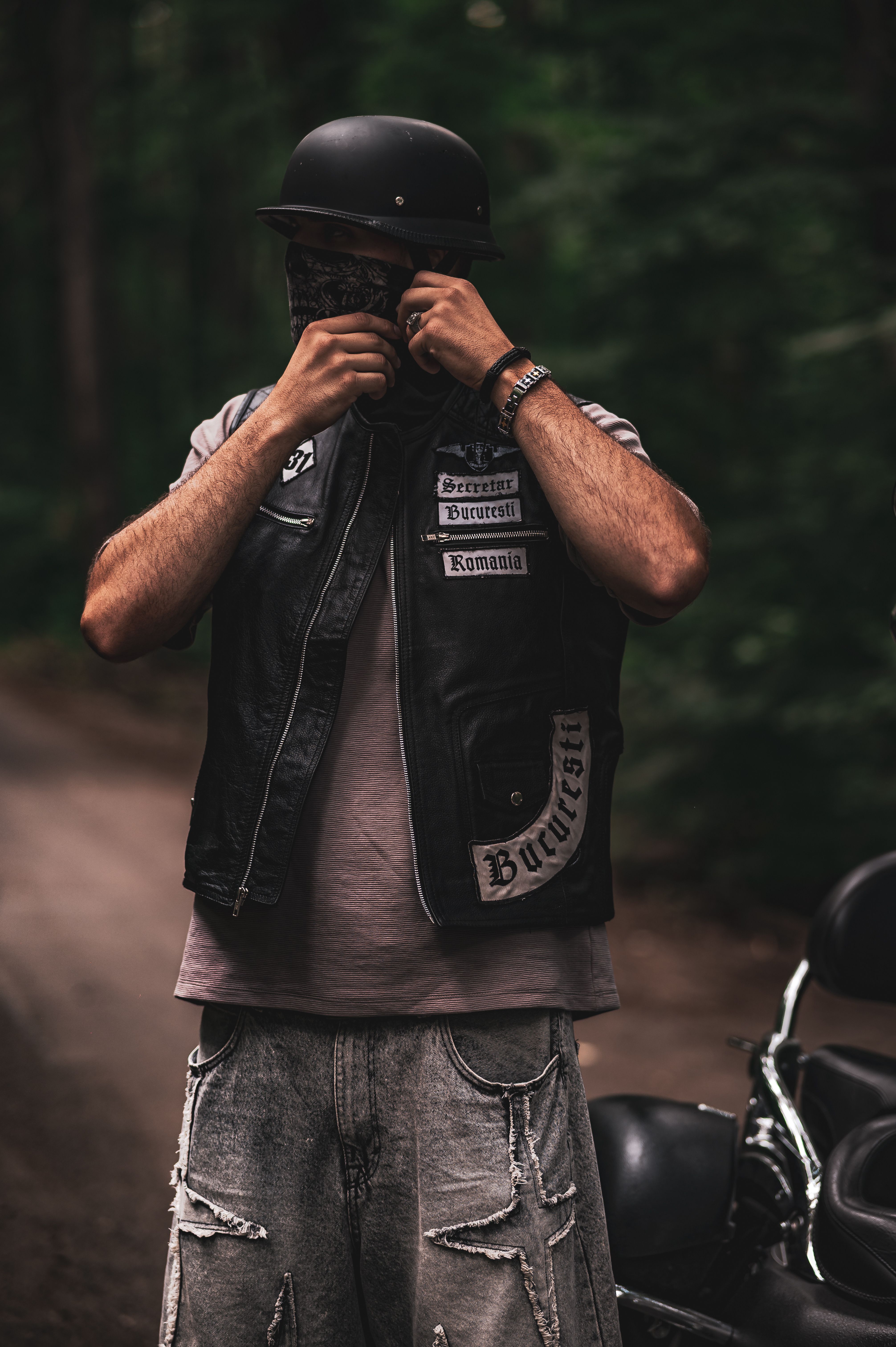 Man wearing a biker outfit adjusting his bandana in a forest setting.