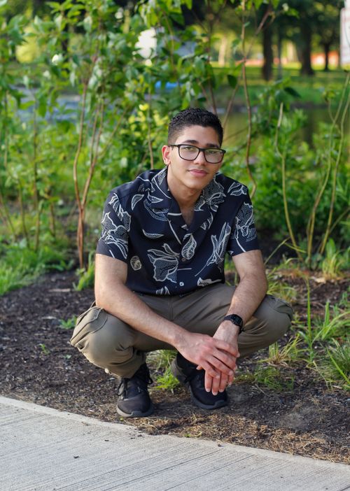 Free Man wearing tropical shirt squatting on a pathway with greenery at daytime. Stock Photo