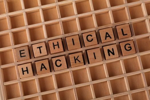 Wooden letter blocks spelling 'Ethical Hacking' on a grid background, symbolizing cybersecurity.