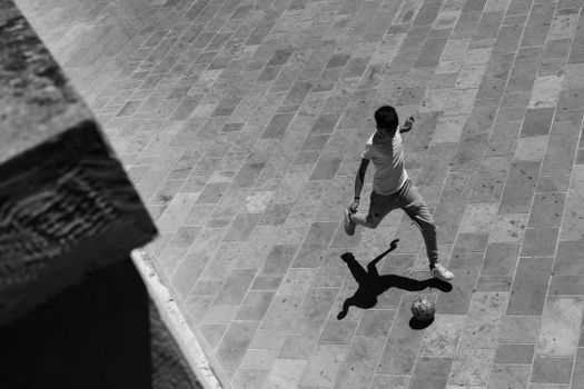 Aerial view of a boy kicking a soccer ball on a tiled surface, in black and white.