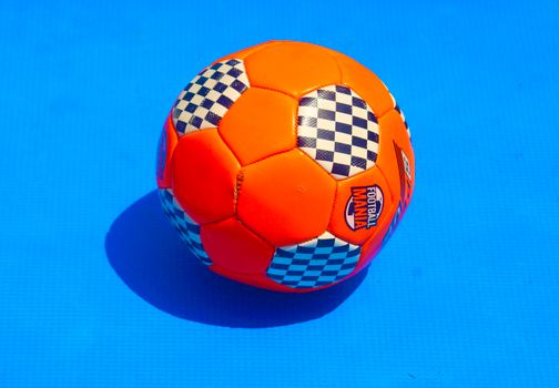 Orange soccer ball with checkerboard pattern on vivid blue background.
