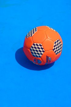 Close-up of an orange soccer ball with checkered pattern on a vibrant blue surface, perfect for sports themes.
