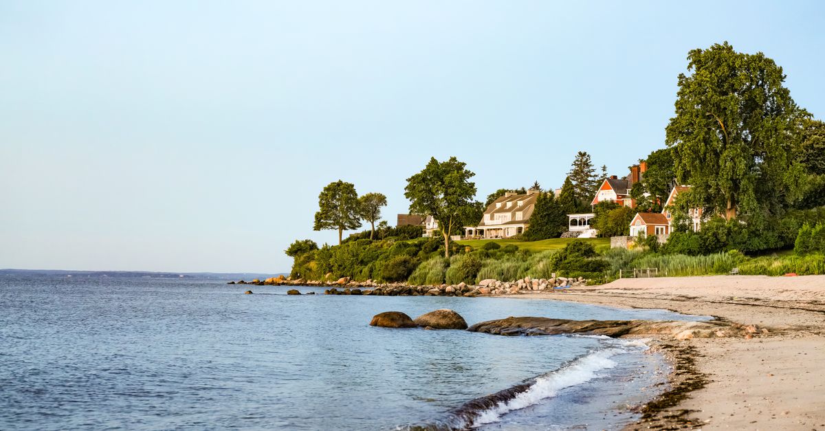 Charming seaside homes overlooking a tranquil sandy beach at sunset.