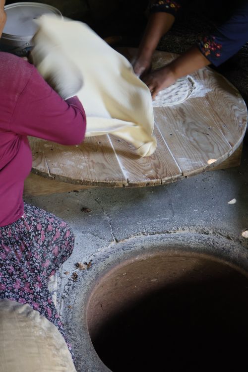 Free Two women prepare traditional flatbread dough over a pit oven indoors. Stock Photo