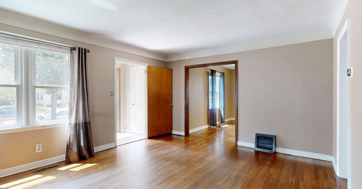 Empty living room with hardwood floors and large windows for natural light.